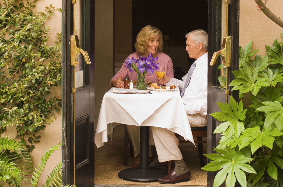 A retired couple dine in an upscale cafe in Charleston, South Carolina. The doors in front of their table are open, allowing the couple to enjoy the beautiful weather as they dine.