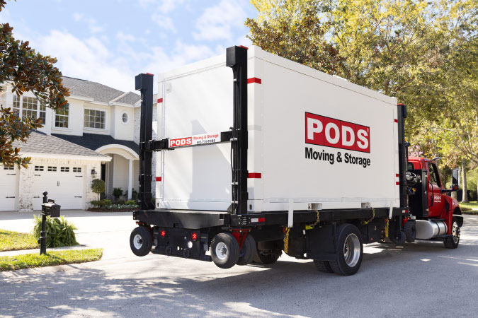 A PODS truck is stopped outside a residential home as the driver prepares to deliver a portable moving and storage container.