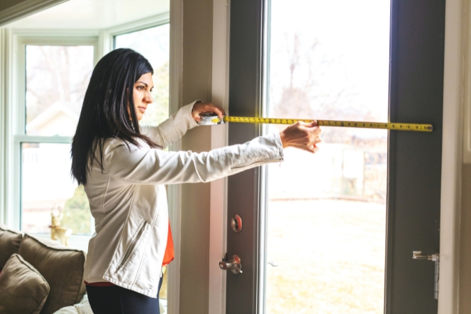 A woman measuring her front door with one of the best tools to move heavy furniture — a measuring tape — ensuring that her furniture will actually fit through the doorway.