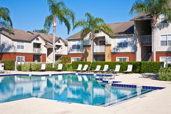 An apartment community with a resort-style swimming pool, palm trees, and multi-story residential buildings, perfect for residents living in Clearwater, FL.