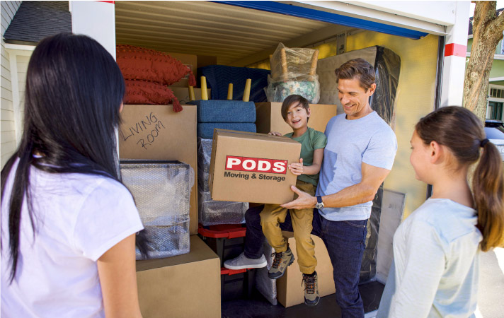 A happy family of four is gathered by the door of their loaded PODS moving container. 