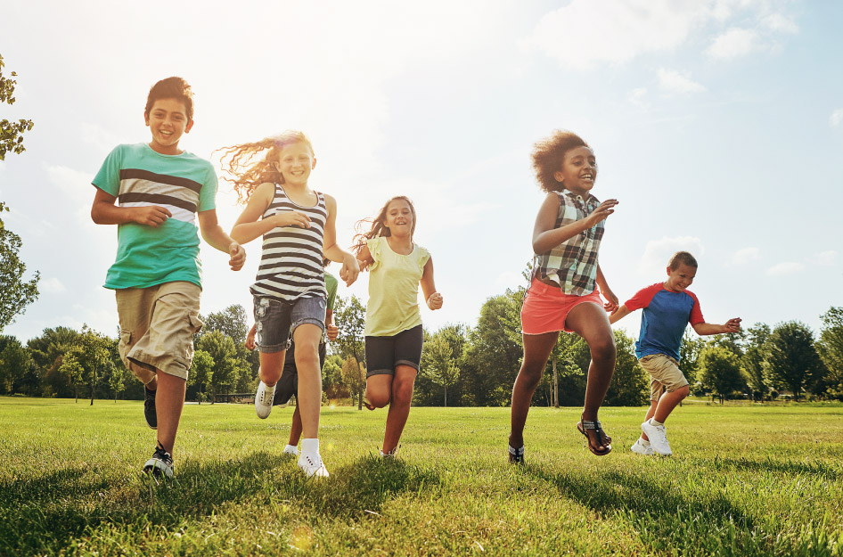 A group of kids are running happily through a grassy field.