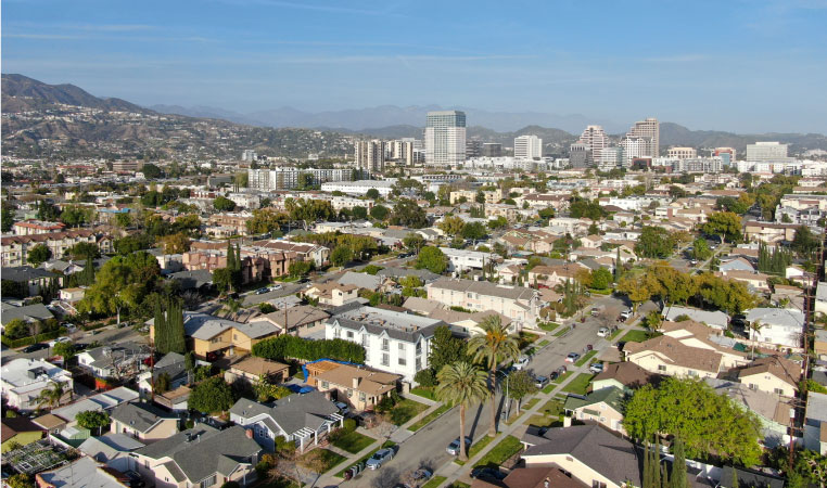 Aerial view of downtown Glendale, California, with rows of residential buildings in the foreground and mountains in the background.