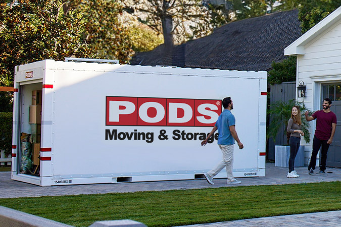A family is hanging outside of their new home near a full PODS portable moving container, taking their time before unloading everything inside.