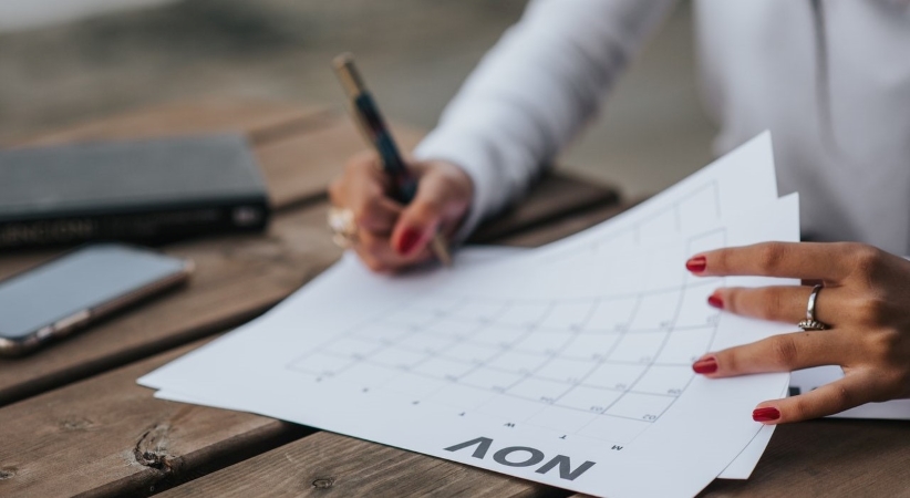 Close-up view of a woman marking a printed-out calendar as she works her way through the steps of her moving checklist (apartment-edition). 