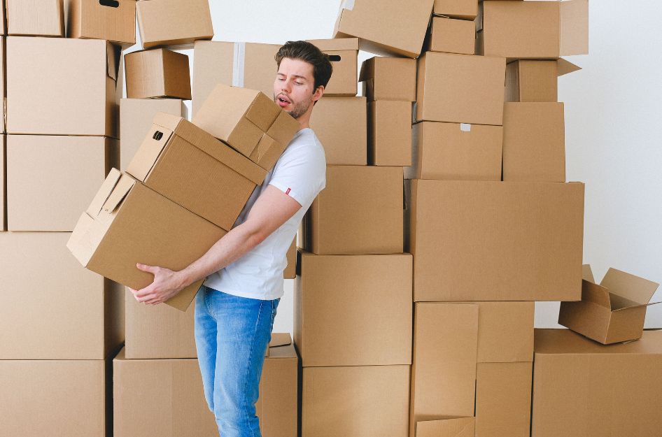 A man leans back as he carries moving boxes that he got for free while surrounded by many others.