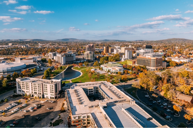 Aerial view of the Big Spring Park area of downtown Huntsville in Alabama — one of the best Southern states — featuring tall city buildings and trees with fall foliage in the distance.