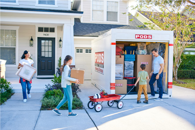A family of four works together to carry items out of their house to the PODS portable moving container in their driveway as they prepare to move to Virginia Beach