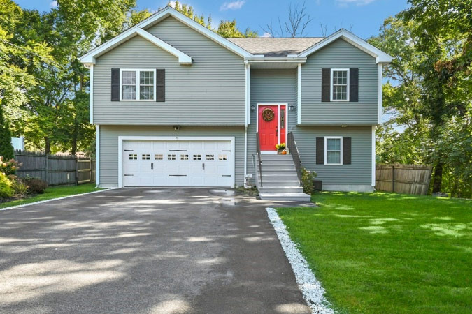 A split-level home in Webster Square — one of the best Worcester neighborhoods — featuring a two-car garage, red door, and shady lawn.