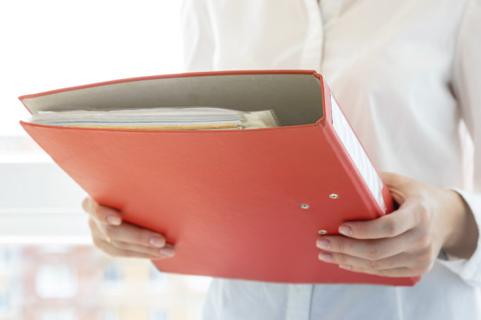 A woman is holding a red binder that she’s using to organize moving documents — step one of her long-distance moving timeline.