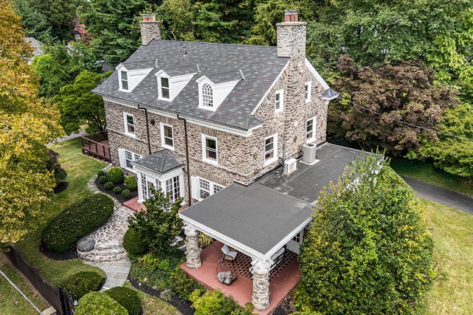 A stone mansion in Mt. Airy — one of the safest neighborhoods in Philadelphia — featuring twin chimneys, a covered porch, and lush landscaping.