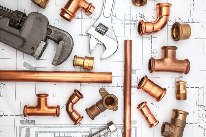 An array of pipes, wrenches, and pipe fittings are resting atop plumbing plans