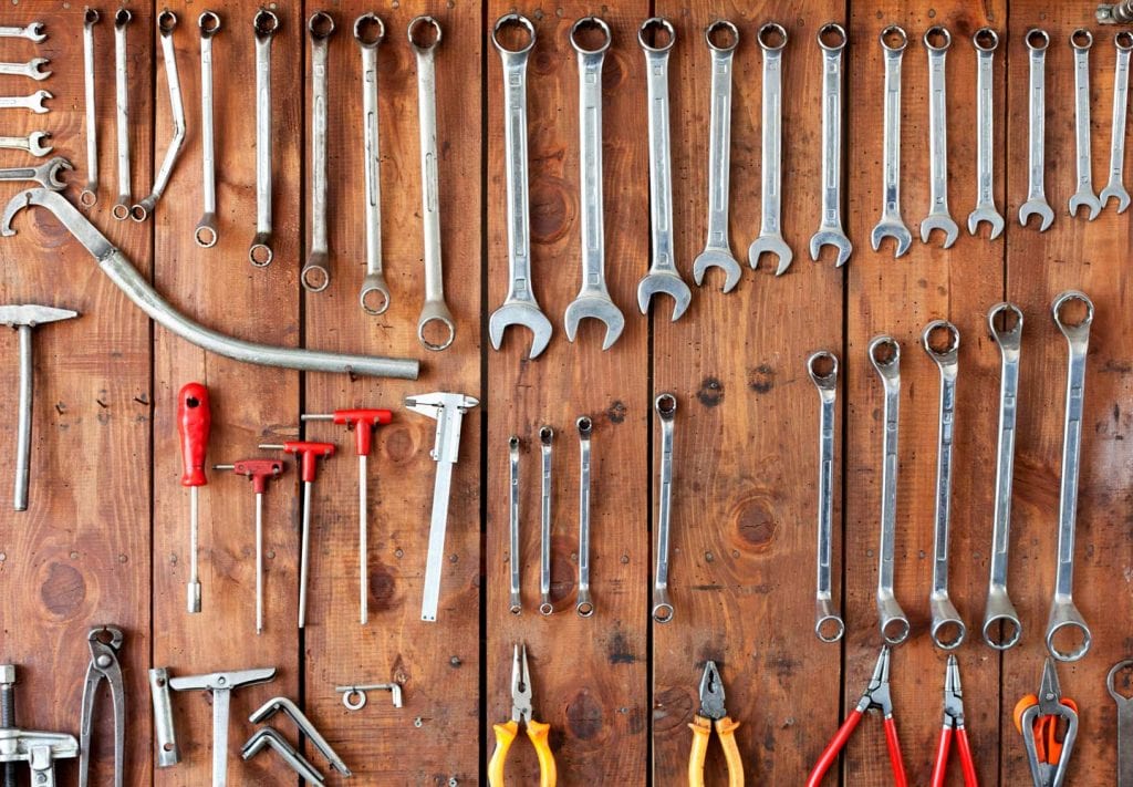 A close up of a wall of tools. There are different types of wrenches and screwdrivers and plyers hanging up.