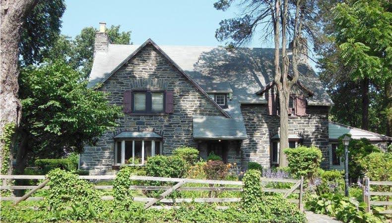 A stone, colonial home in Ardmore, Pennsylvania — one of the towns near Philadelphia — featuring an overgrown yard with creeping vines on the fence.