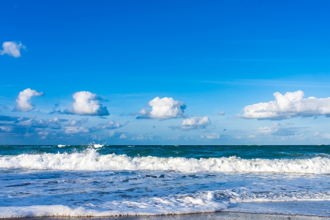 Beach waves crashing onto the shore with foamy suds beneath a bright blue sky at a beach in Melbourne — the perfect place to find outdoorsy things to do in Melbourne, FL.