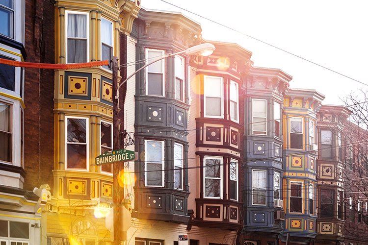  Colorful row houses with ornamental flourishes in Philadelphia, PA. There is a green sign that reads “Bainbridge St.”