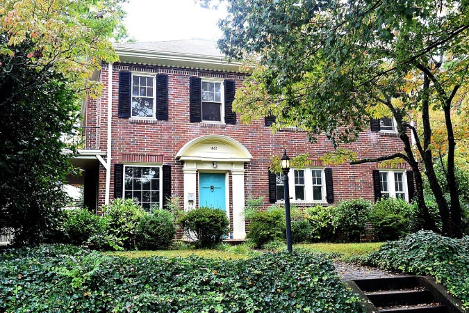 A beautiful, two-story brick home in West Highlands — one of the best Winston-Salem neighborhoods — featuring an arched entryway and a blue door.