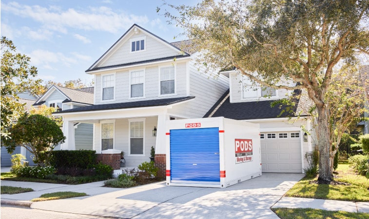 A PODS moving and storage container in the driveway of a two-story residential home.