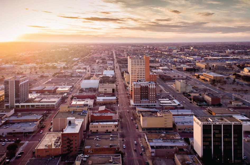 Aerial view of Lubbock, Texas, during sunrise, featuring a relatively flat landscape, and a spattering of tall city buildings amid hundreds of squat structures.