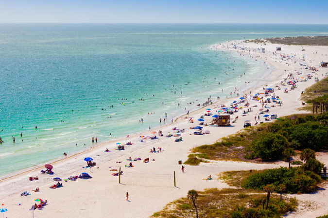 Distant view of hundreds of beachgoers enjoying a sunny day at Lido Beach in Sarasota, FL — the No. 1 most moved-to city in the U.S. in 2025. 
