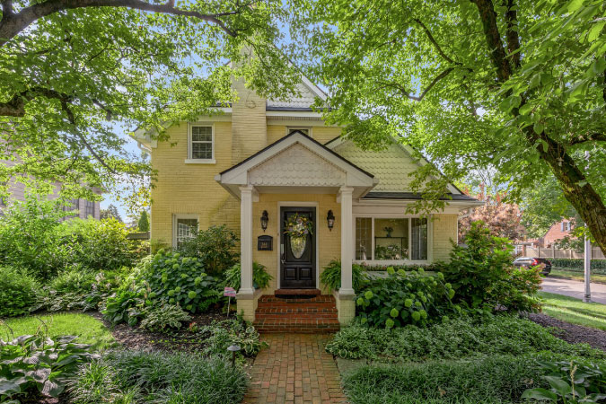A quaint, yellow house in Chevy Chase — one of the best neighborhoods in Lexington, KY — featuring a brick entry path, covered stoop, and three front-facing gables.