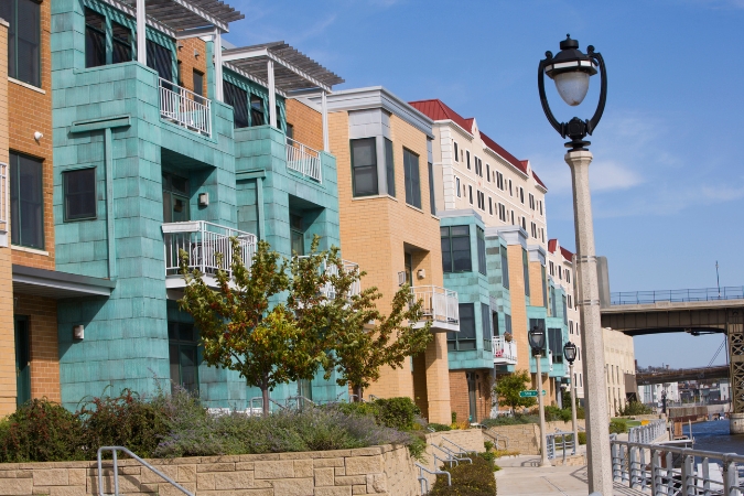 Brightly colored condos line the Milwaukee River alongside a paved pedestrian pathway, highlighting the appeal of living in Wisconsin's vibrant urban communities.