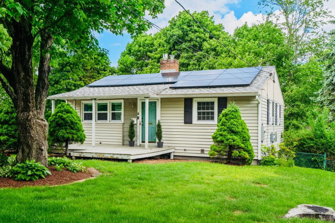 A charming ranch-style home in Tatnuck — one of the best Worcester neighborhoods — featuring solar panels on the roof and a lush, green lawn.