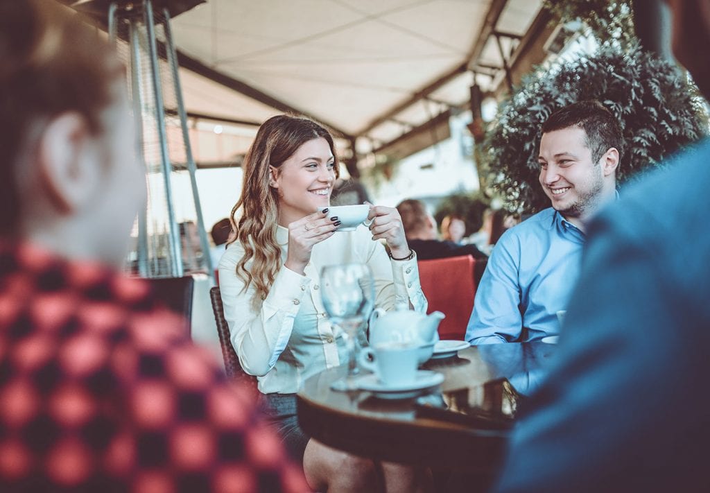 A group of friends gather at a restaurant table, drinking tea and talking