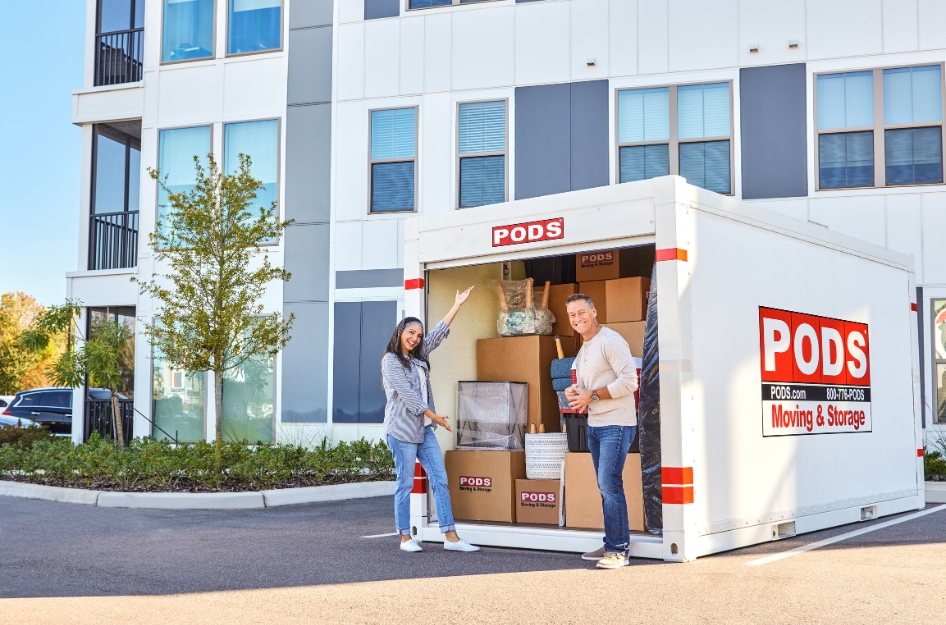 PODS Apartment delivery at a modern apartment building, with two people standing beside an open PODS portable storage container filled with packed boxes and household furniture.