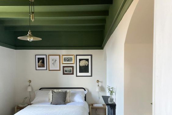 a bedroom with a green cieling and black bed frame with white bedding and photos on the wall. 