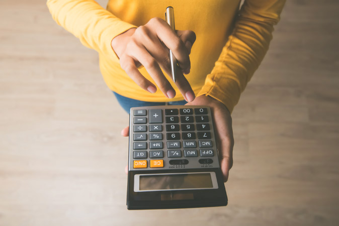 Close-up view of a calculator being held by a woman in a long-sleeved yellow shirt as she calculates PODS vs. moving company costs.