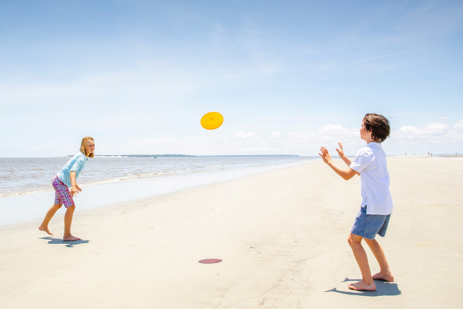 Two young kids play frisbee on a Jekyll Island beach in Georgia on a sunny day.