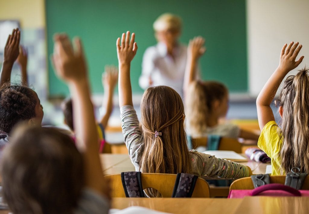 Young students voulenteer their answers and raise their hands in class. 