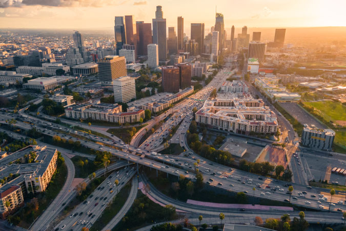 Aerial view of the Downtown Los Angeles skyline just before sunset, featuring an intricate maze of freeways and overpasses.