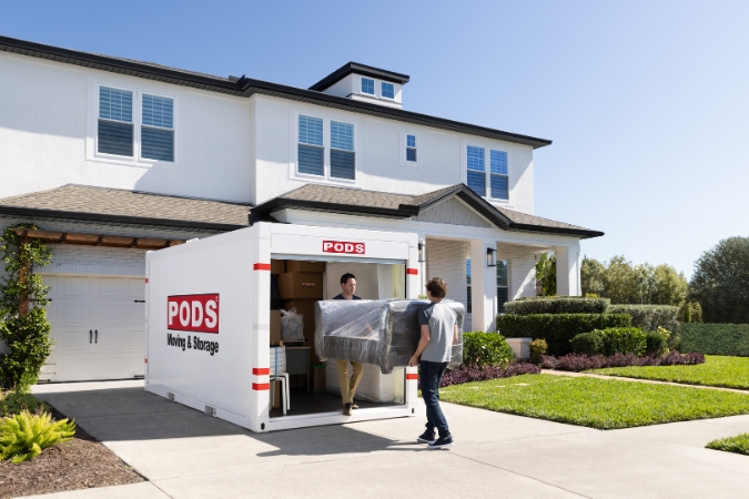 A father and son carry a wrapped couch into a PODS portable moving container sitting outside of a home, one of the best moving options for an estate move. 