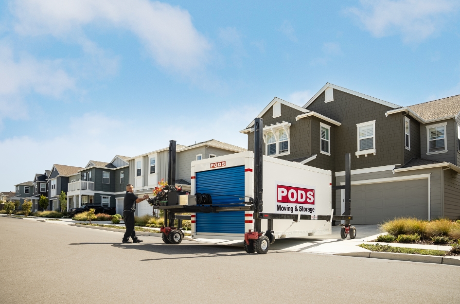 A PODS driver is using PODZILLA to position a portable storage container in a residential driveway — an example of self-storage with pickup and delivery service.
