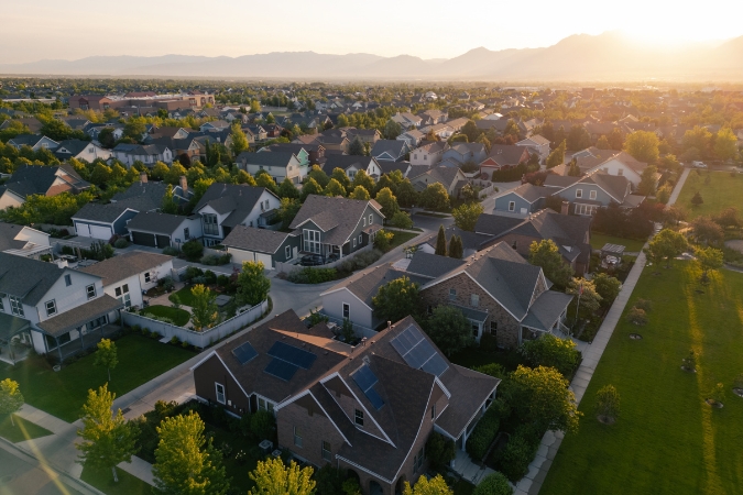 An aerial view of a suburban neighborhood with large, modern homes surrounded by lush foliage and distant mountains.