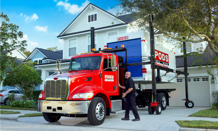 A PODS driver is standing beside his truck in a residential driveway.
