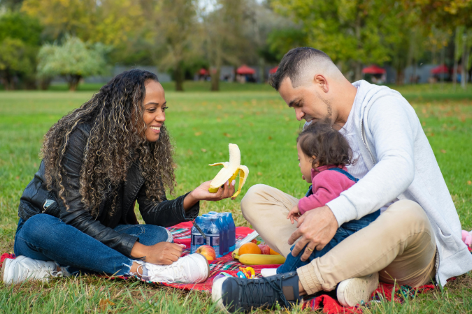 A young family of three sit in the park enjoying a picnic after moving to a sunnier climate.