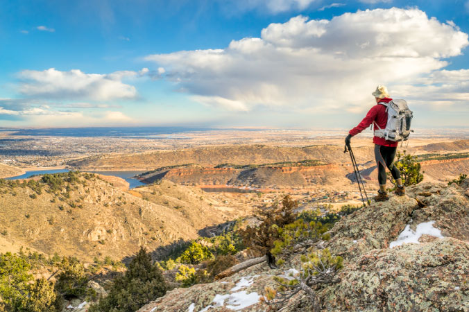 A backpacker with hiking poles takes a moment to enjoy the breathtaking view from a mountain ridge above Fort Collins, Colorado, on a clear winter day.