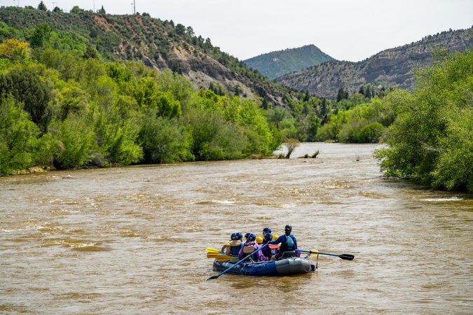 A group of people living in Durango, CO, embark on a rafting trip down the Animas River, surrounded by lush mountains on both sides.
