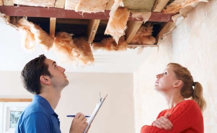 A woman and a contractor look at ceiling damage. The man checks things off a checklist on a clipboard.