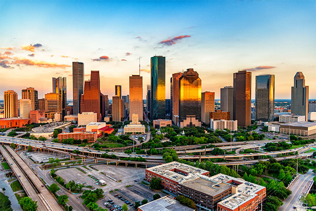 The skyline of Houston, Texas, at sunset. It reflects off the skyscrapers as cars drive on the roads below.
