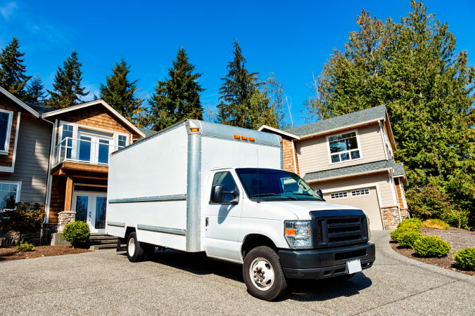 A white moving truck rental parked in front of a residential house, ready to be loaded.