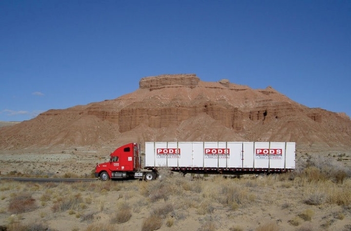 A PODS truck carrying three portable storage containers is driving through the red rocks of the western United States.