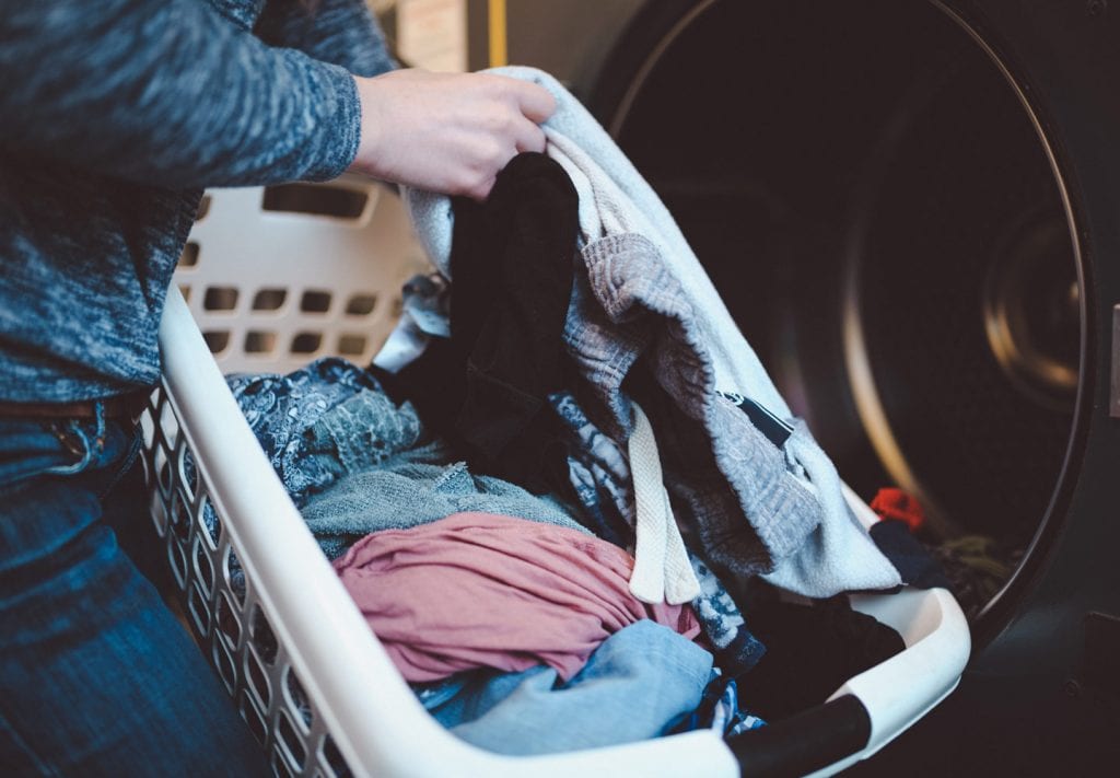 A close-up view of a laundry basket as a woman transfers clothing into a washing machine to clean it before storing clothes. 