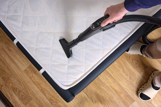 View from above of someone vacuuming a mattress.