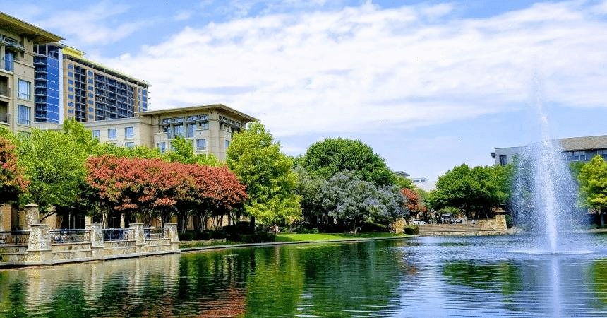 A large water feature at The Shops at Legacy in Plano, Texas, is surrounded by colorful trees and large buildings. 