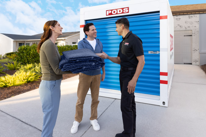 A couple is speaking with a PODS driver in front of a PODS portable storage container in their driveway.