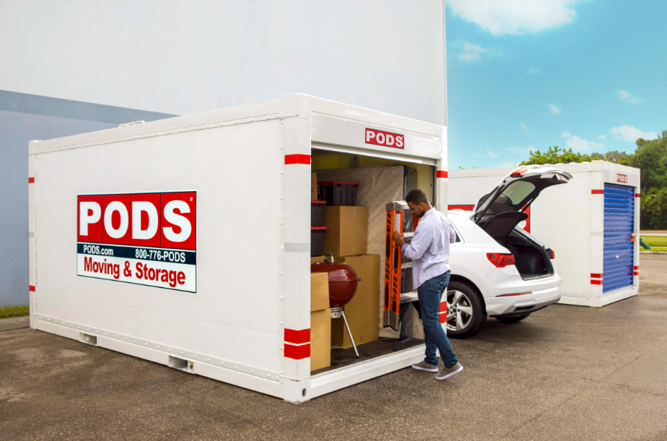 A young man unloads things from his car and packs his PODS portable storage container as he prepares to ship his car in his move.